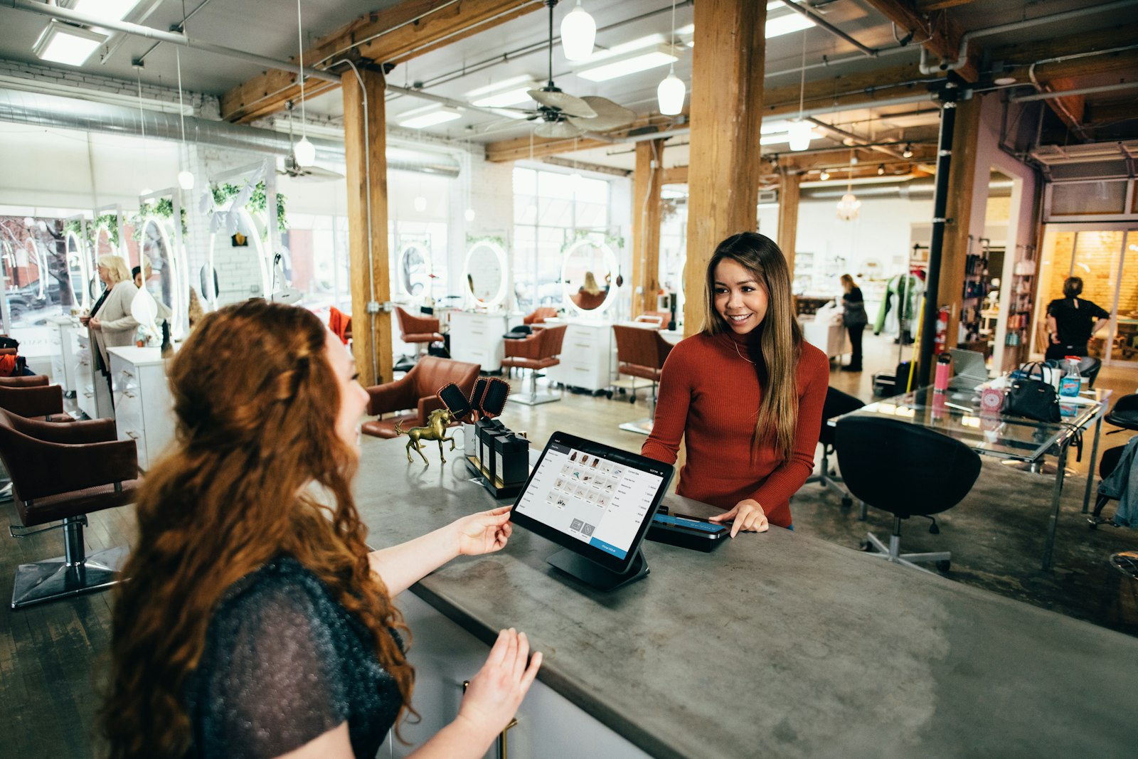 Une réceptionniste accueille une cliente au comptoir, ordinateur ouvert